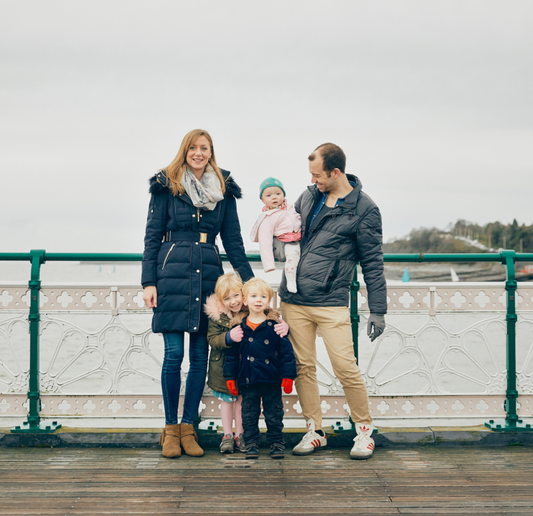 Un homme et une femme avec leurs trois enfants debout contre la rambarde d'une jetée.