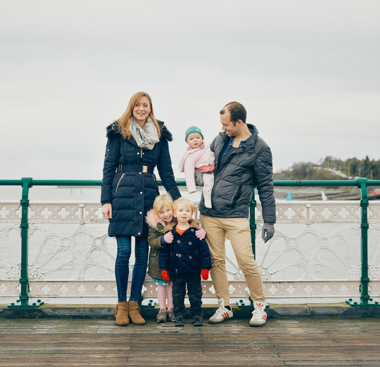 A man and a woman with their three children standing against the railing of a pier