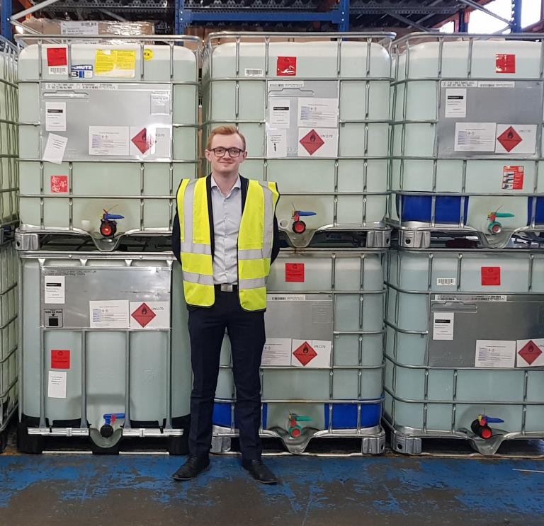 A man in a warehouse stands in front of large industrial sized containers of liquid