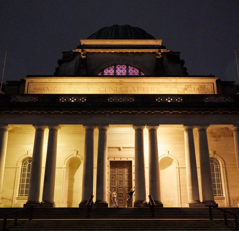 Außenansicht eines Eingangs in ein großes Museumsgebäude, bei Nacht erleuchtet.