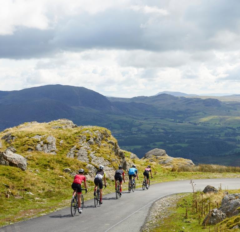 Cinq cyclistes descendent une route pittoresque avec des montagnes en toile de fond.
