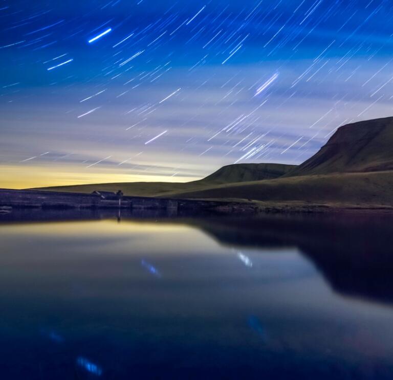 A night shot of a lake and some mountains with starry skies behind