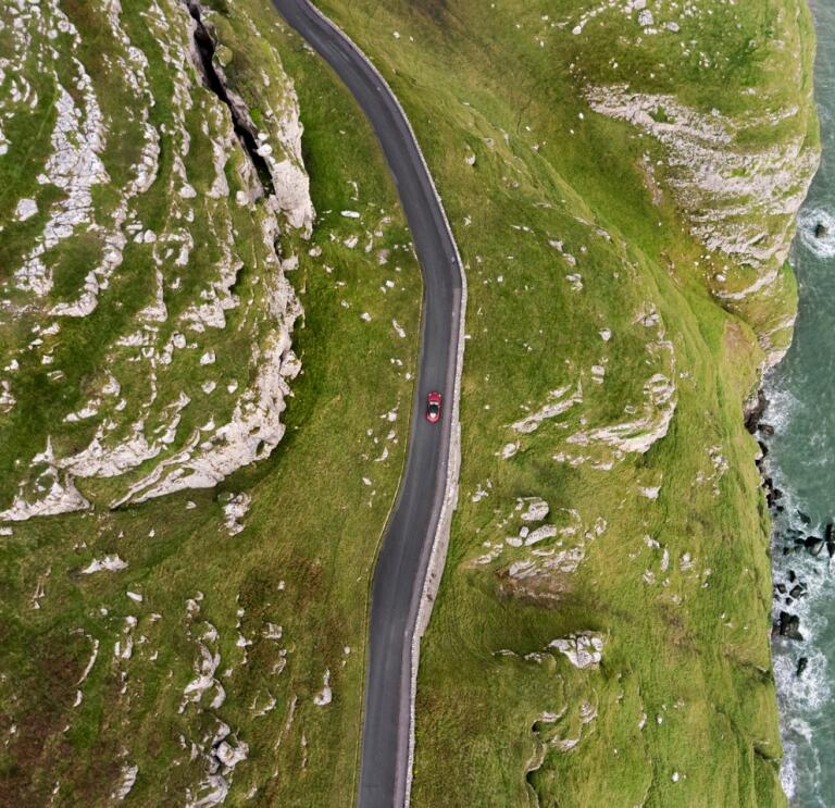 An aerial shot of a car driving along a mountainous coastal road 