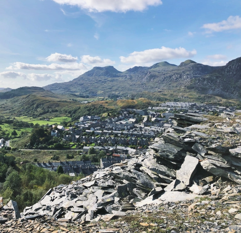 A mountain of slate in the foreground, with terraced houses and further mountains in the background