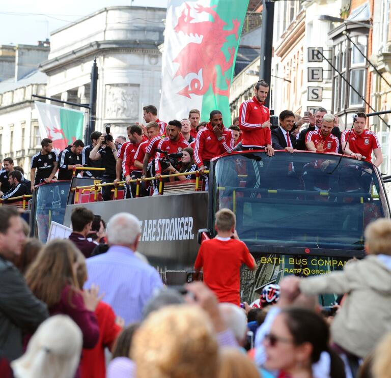 The Wales football team on top of their tour bus waving at crowds below.