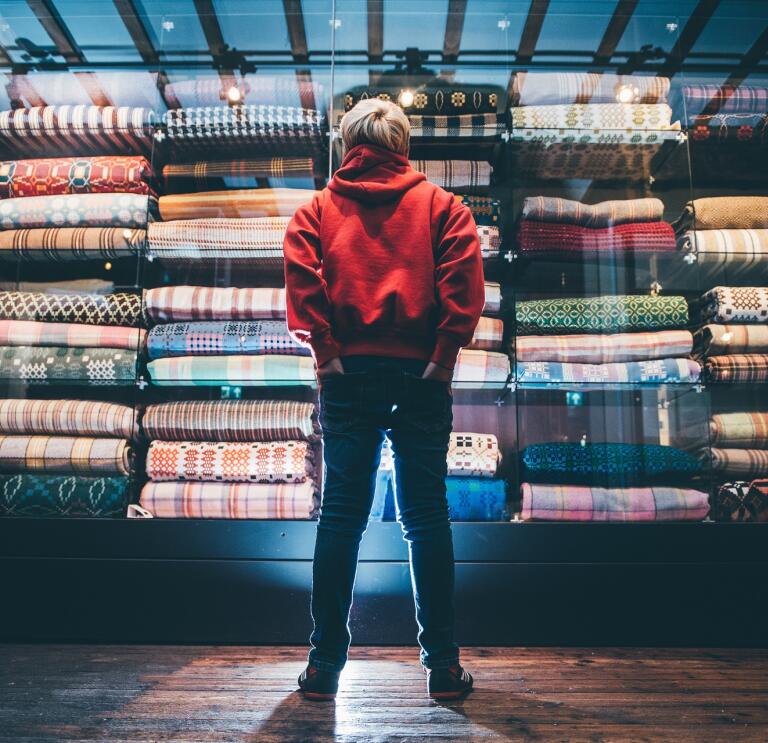 A young boy looking up at a colourful cabinet full of Welsh blankets.