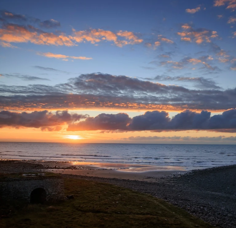 Una hermosa y colorida puesta de sol vista sobre una extensión de playa y costa.