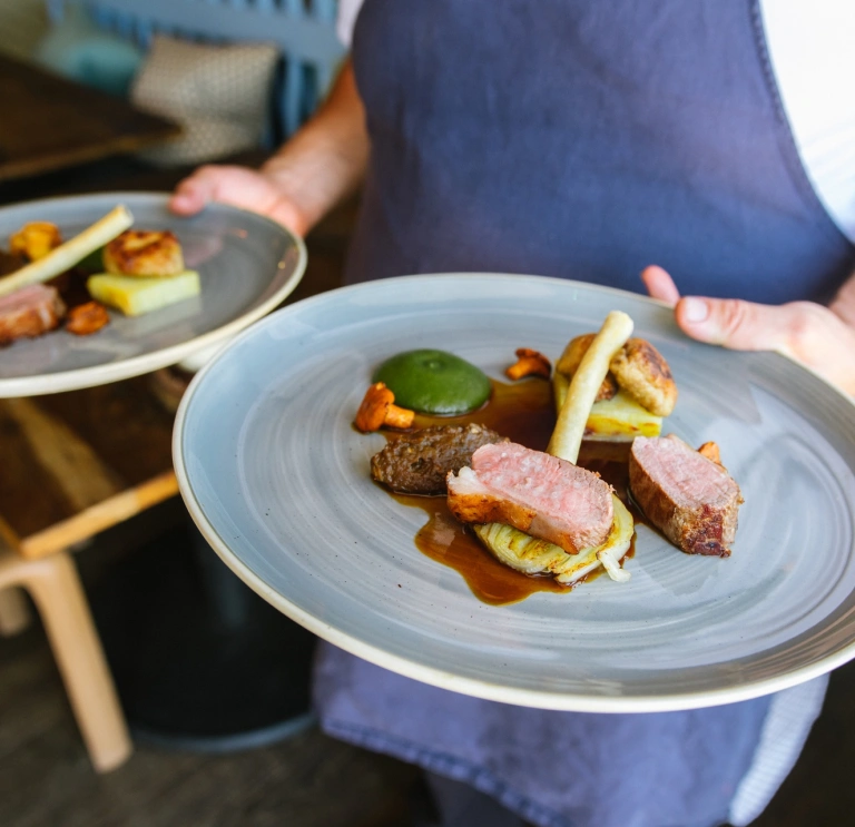 Un chef cuisinier porte deux assiettes de nourriture.