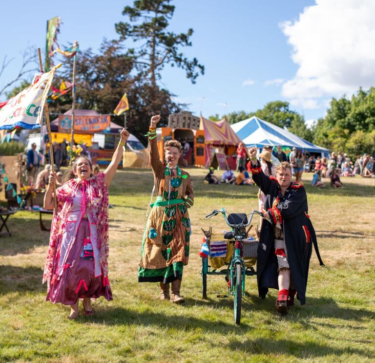 Three people dressed in bright festival costumes raising their arms to wave 
