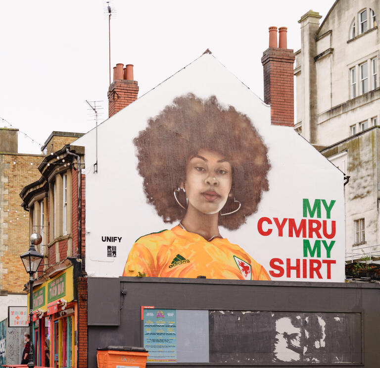 A huge mural of a woman wearing a yellow football shirt, on the side of a building.