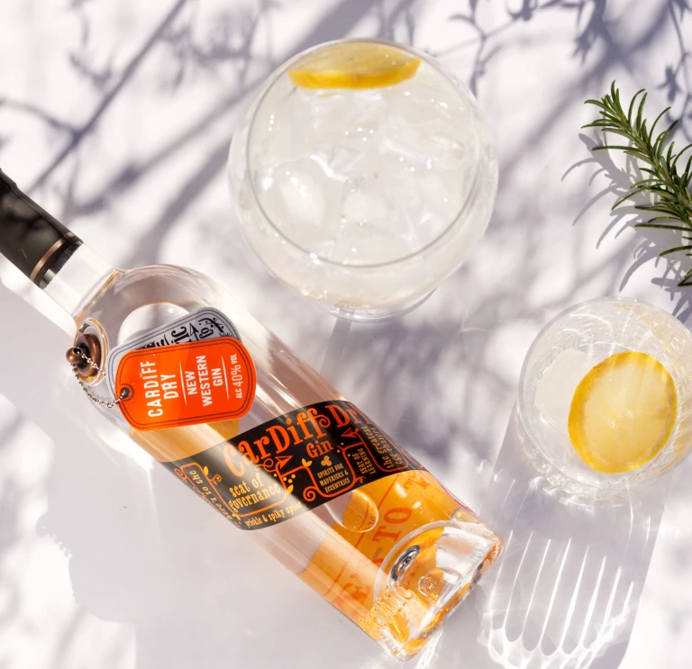 A bottle of Cardiff Dry Gin, set next to botanicals and a poured glass with ice