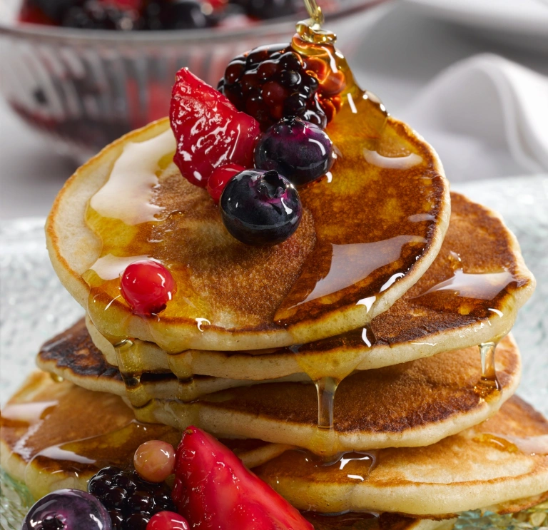 A pile of crempog (Welsh pancakes) with berries and syrup
