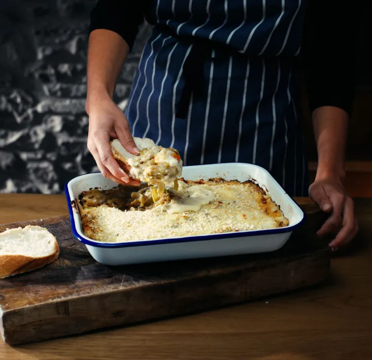 Un plat à rôtir contenant des œufs d’Anglesey fraîchement cuits, avec la main d’un chef en train d’en servir une portion sur une tranche de pain coupé.