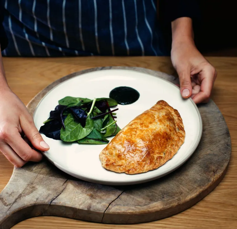 Ein wunderschön angerichteter Teller mit einem walisischen Oggie (Pastete) und Salat auf einem Holzbrett.