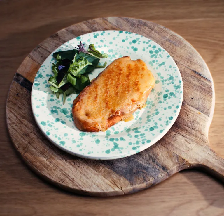 Une assiette de Welsh rarebit (pain grillé avec un mélange au fromage) magnifiquement présentée, avec de la salade, le tout servi sur un plateau en bois.
