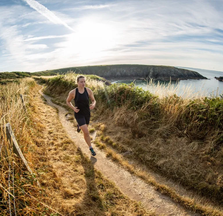 A person running over the cliffs in Pembrokeshire with the sea in the background.
