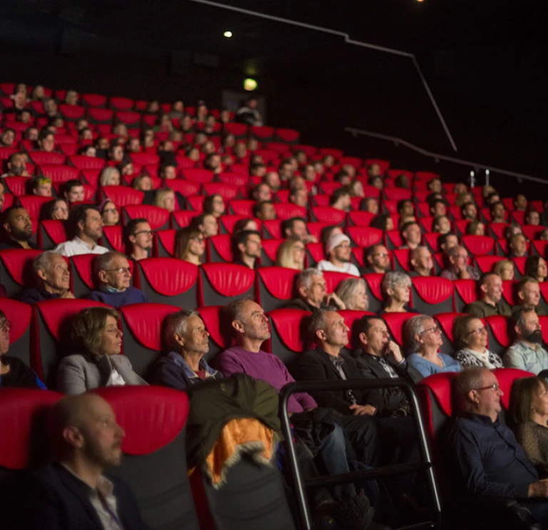 Audience seated in red chairs inside a cinema auditorium