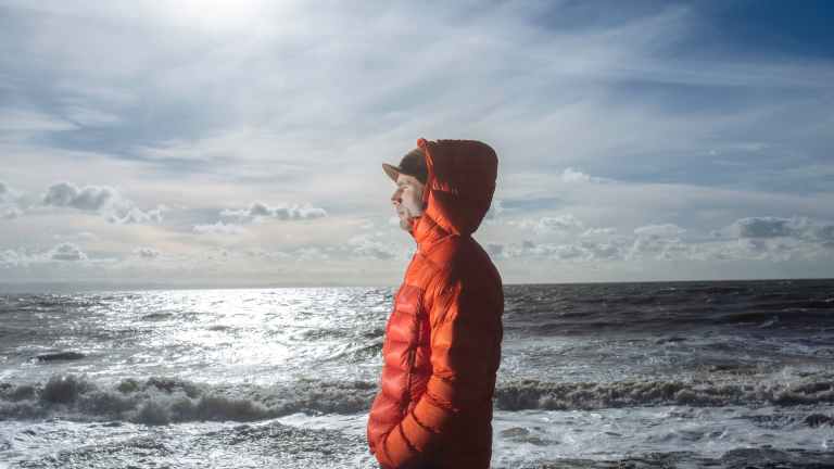 Un hombre con una chaqueta de naranja cálido mirando hacia el mar