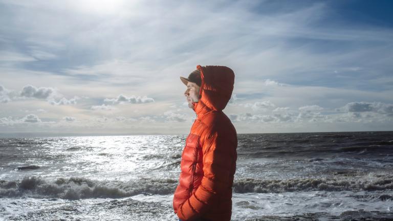 Ein Mann in einer warmen orangefarbenen Jacke, der auf das Meer schaut