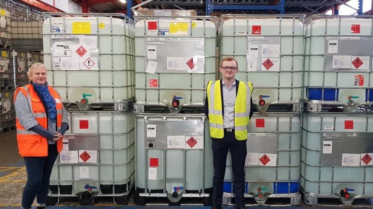 A man in a warehouse stands in front of large industrial sized containers of liquid