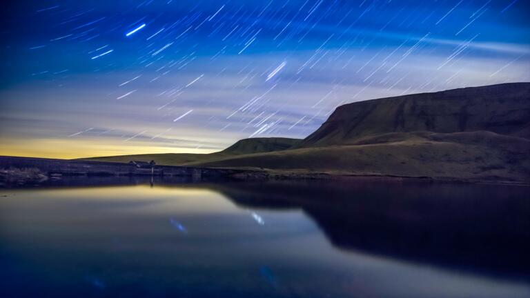 Una toma nocturna de un lago y algunas montañas con cielos estrellados detrás