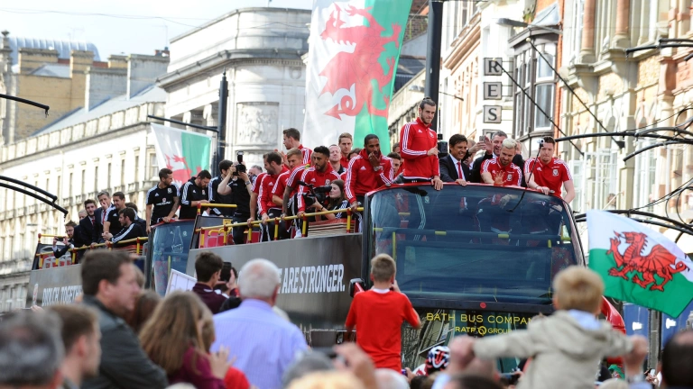 The Wales football team on top of their tour bus waving at crowds below.