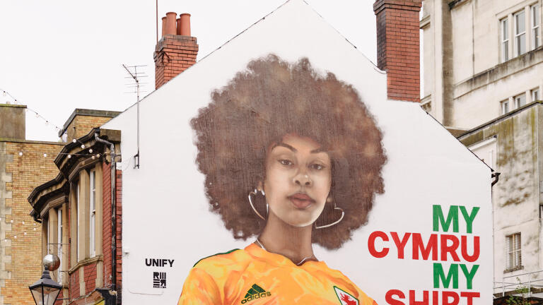 A huge mural of a woman wearing a yellow football shirt, on the side of a building.