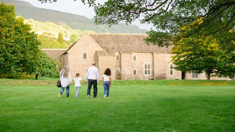 family in field walking towards a stone building.