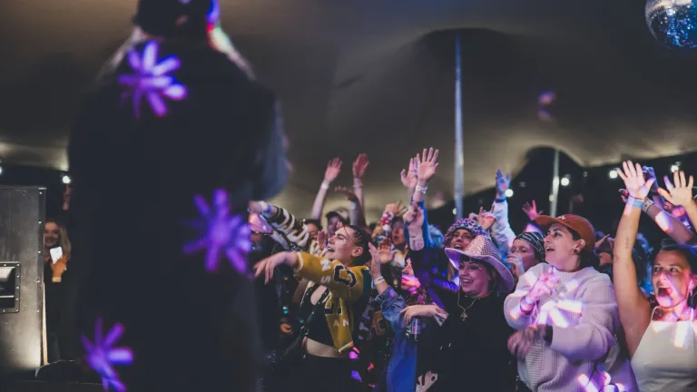 A crowd of people at a festival dancing and singing while looking up at a stage