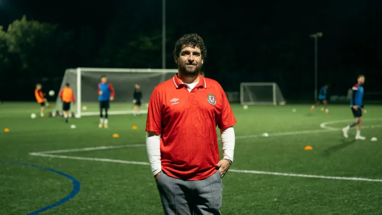 Club founder Delwyn Derrick standing on a football pitch while a game takes places behind him