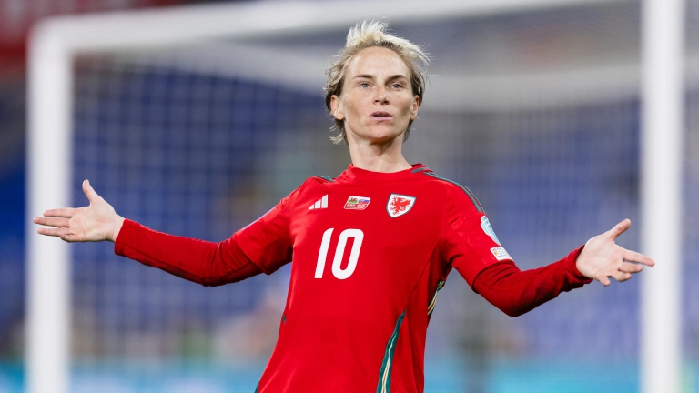 Dressed in her number 10 red football jersey, Fishlock stands with her arms out to her sides with a questioning look on her face 