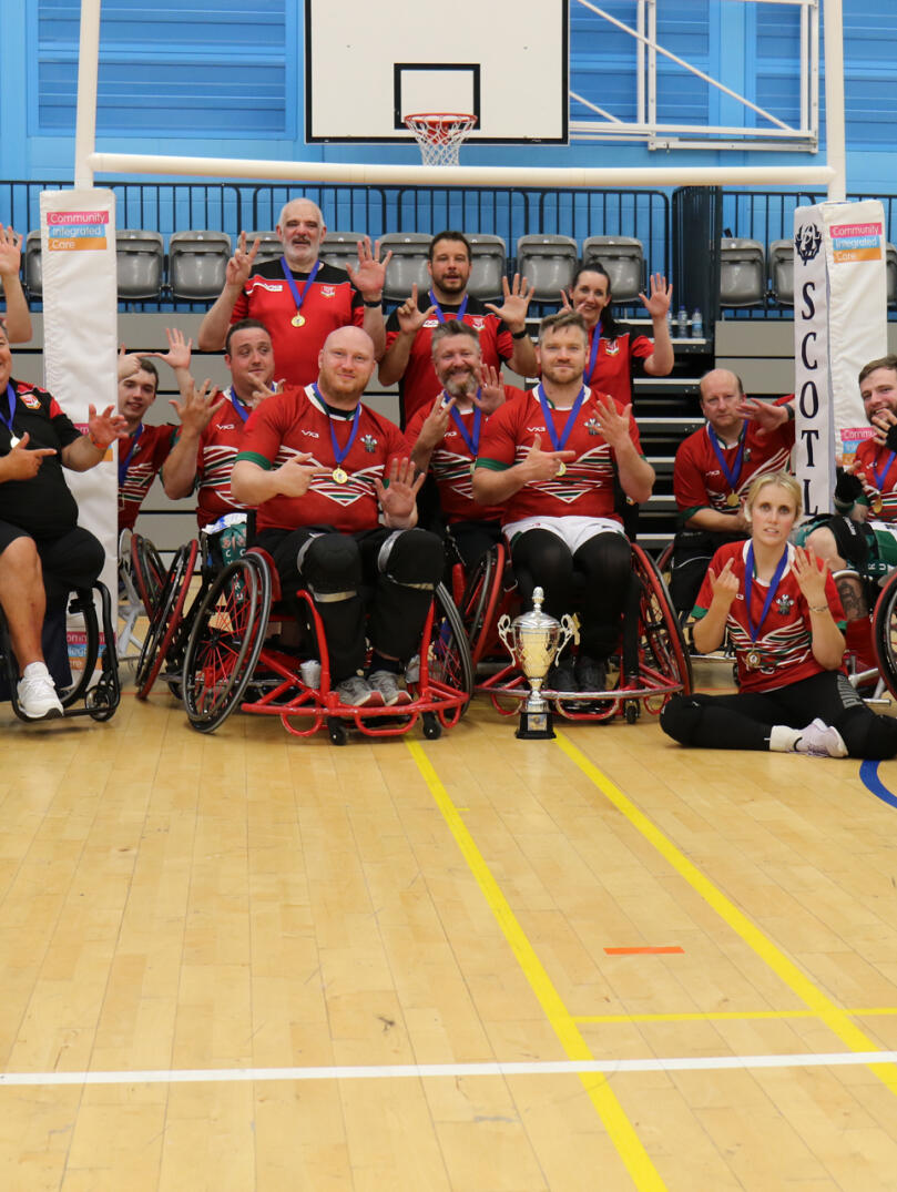 A team of wheelchair rugby players with a silver cup. 