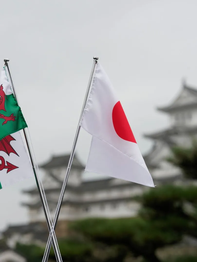 ウェールズの旗と日本の旗が並び、背景には日本の姫路城が美しく広がっている様子