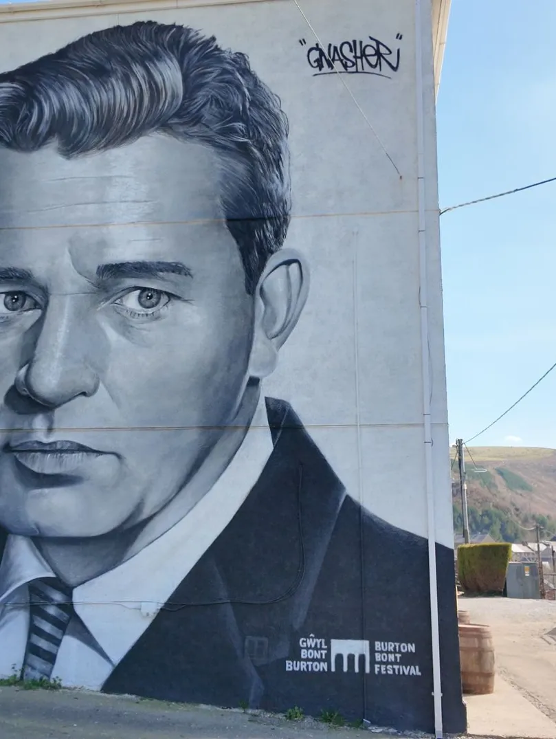 A large painting of Richard Burton on a wall.
