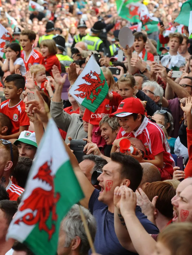A crowd of football supporters holding Welsh flags.