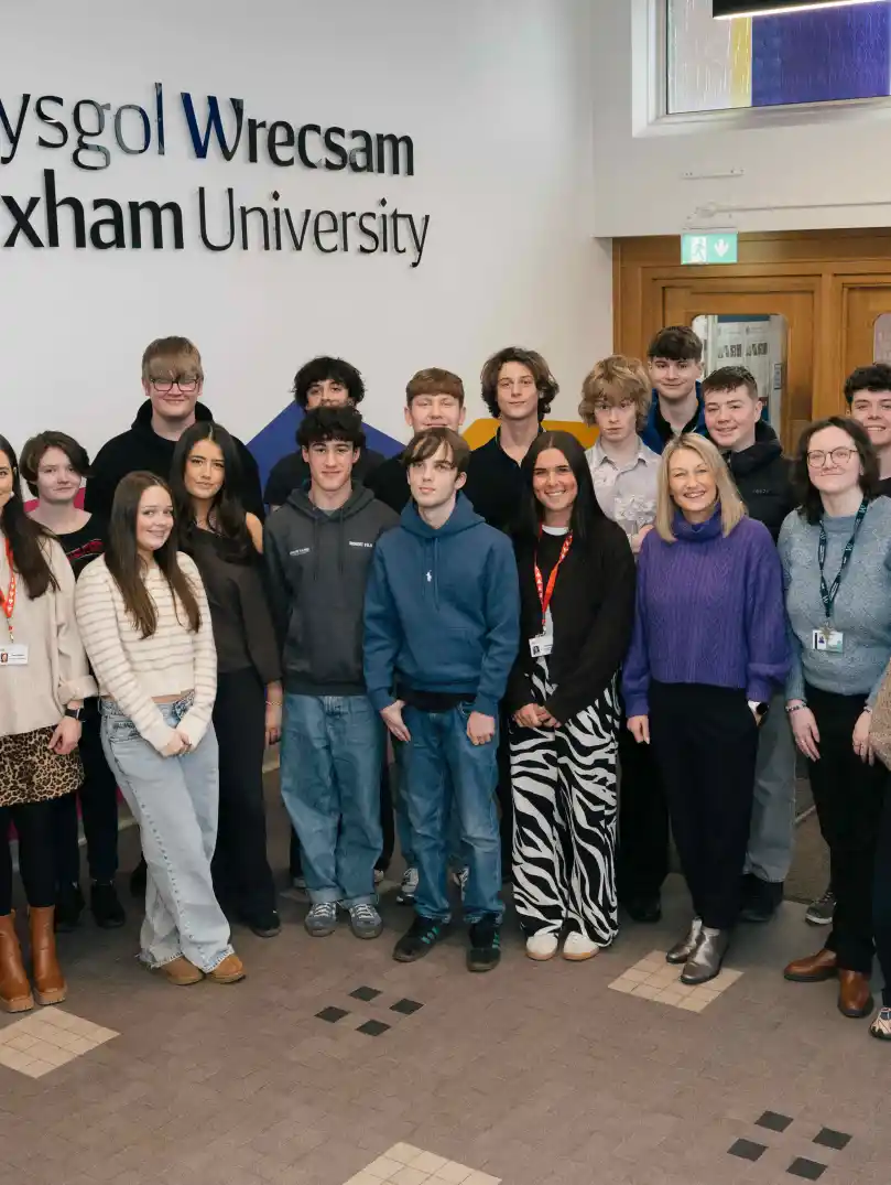 A group of young people and adults standing together inside a university building. They are posing for a group photo in a bright indoor space. 