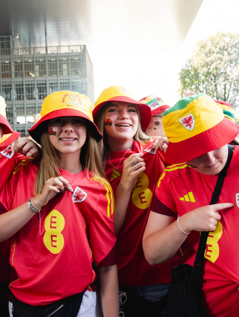Wales supporters wearing Cymru shirts and bucket hats in a UEFA Women's EURO 2025 fan zone. 