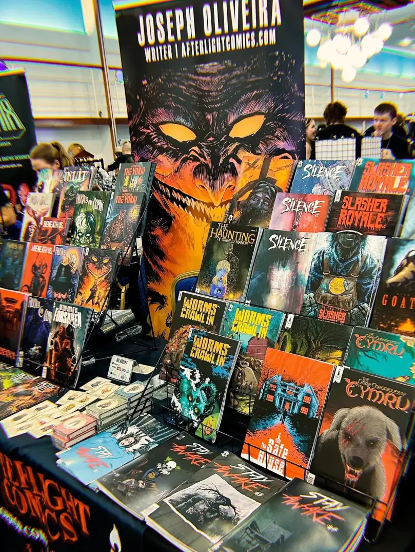 A comic convention stall displaying horror comics and graphic novels by Joseph Oliveira of Afterlight Comics.