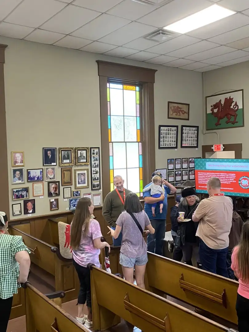 People gather and talk inside a historic building. A presentation screen and colorful windows are visible in the background. 