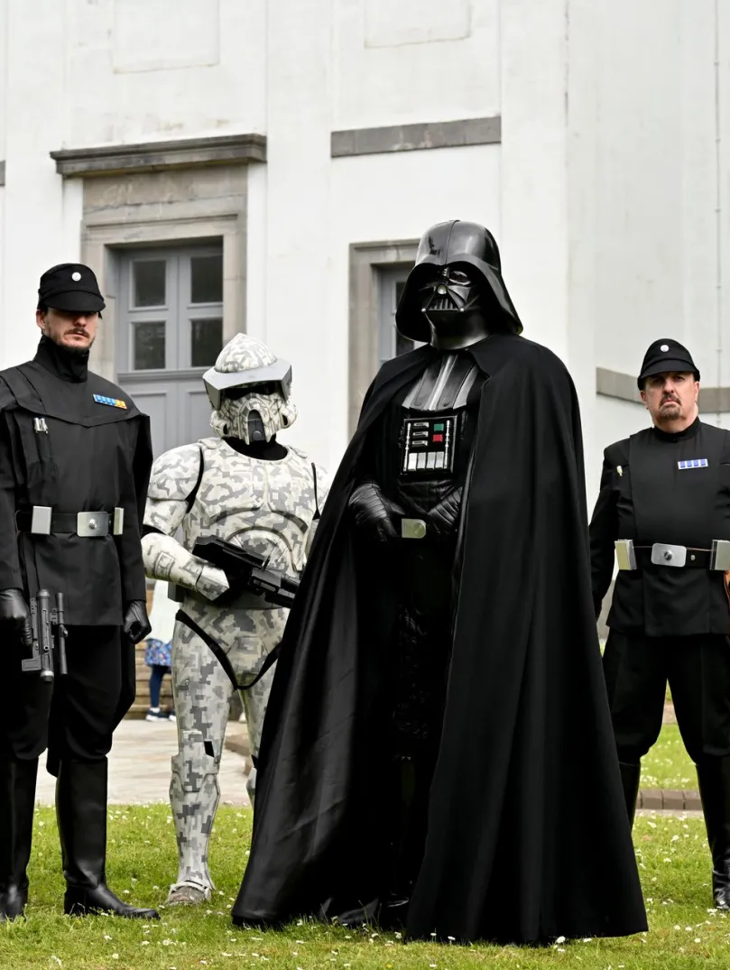 Star Wars characters, including Darth Vader and Stormtroopers, posing outside a white building.