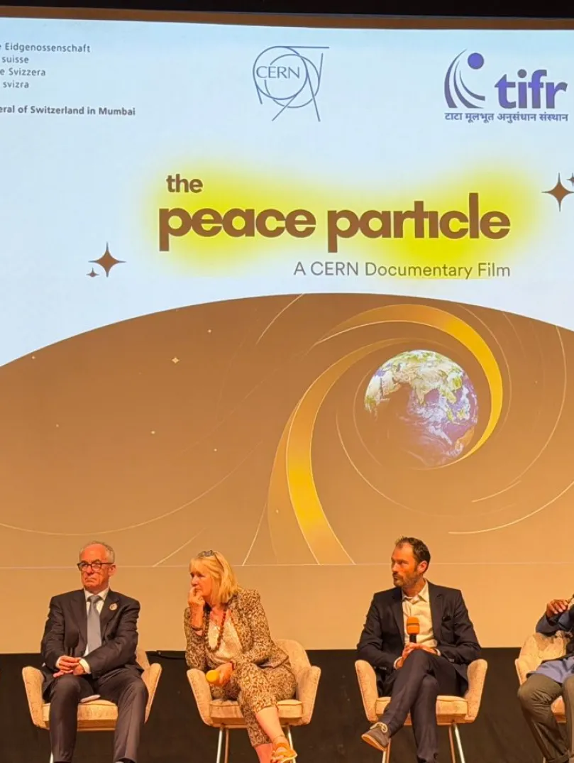 Five panellists seated on stage during a discussion at a screening of The Peace Particle, a CERN documentary film, with the film’s title displayed on a large screen behind them.