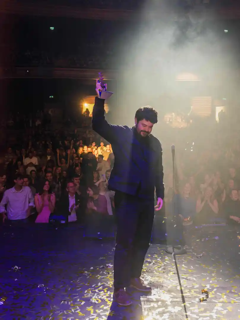 Dafydd Owain holding up his award on stage at the Welsh Music Prize 2026