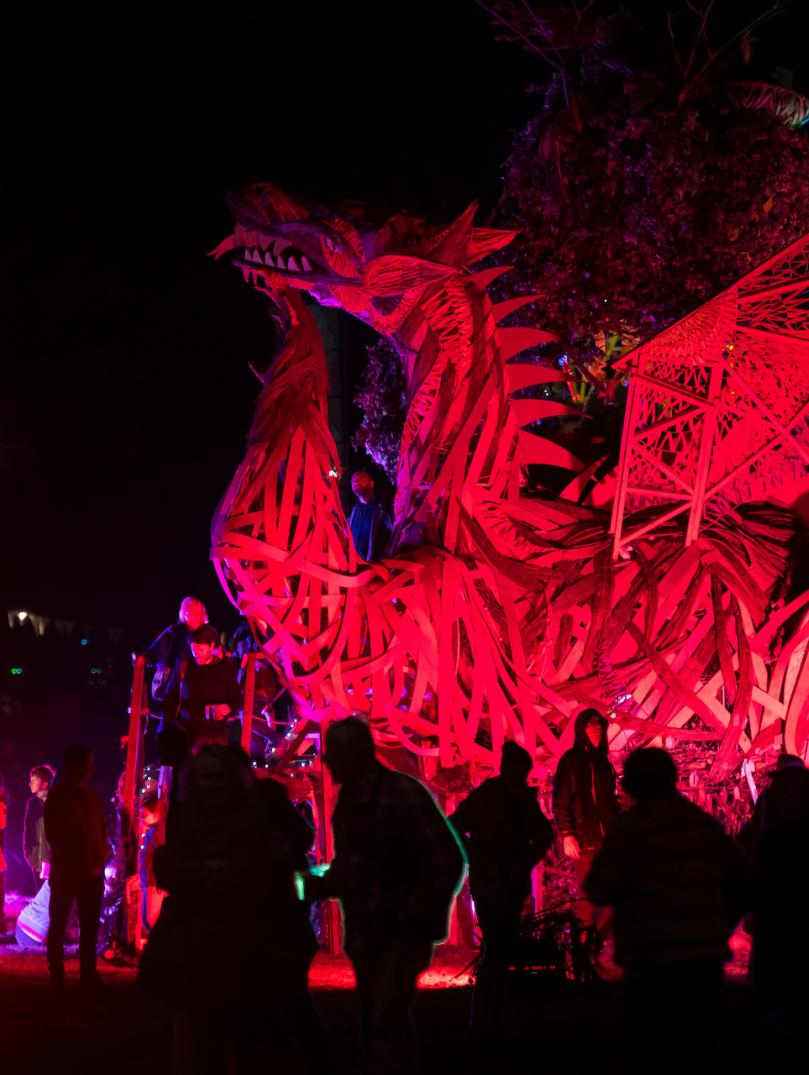 photo de nuit d'une sculpture géante de dragon rouge avec des gens l’observant debout