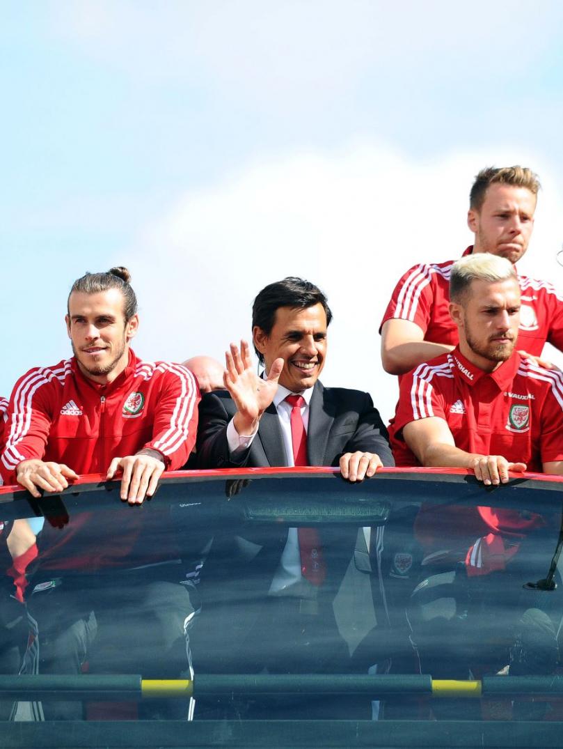 El equipo de fútbol de Gales en la parte superior de su autobús turístico saludando a la multitud debajo.