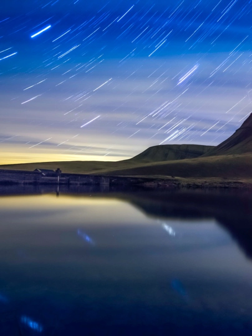Una toma nocturna de un lago y algunas montañas con cielos estrellados detrás
