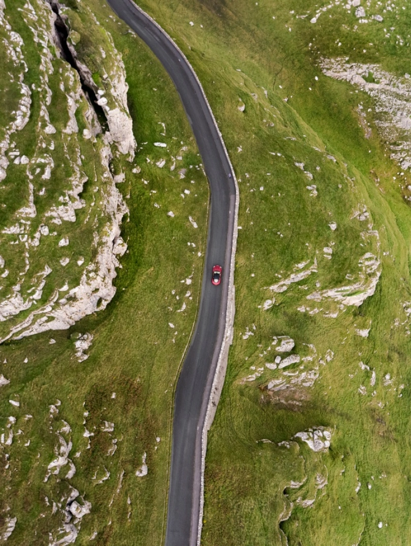 Vue aérienne d'une voiture sur une route côtière montagneuse.