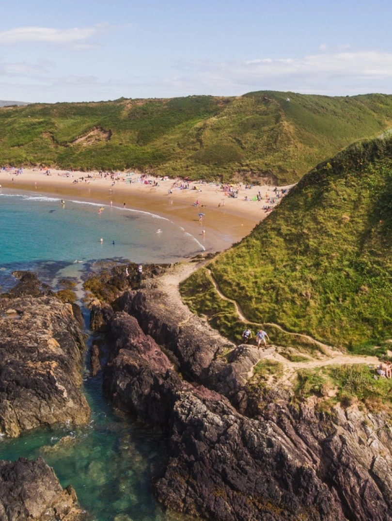 Une baie côtière bleue et sablonneuse entourée de montagnes vertes.