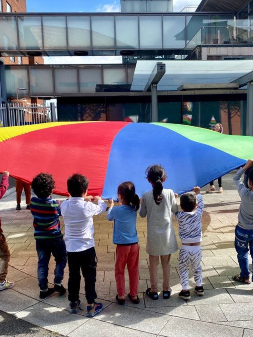 Un grupo de niños jugando con un paracaídas.
