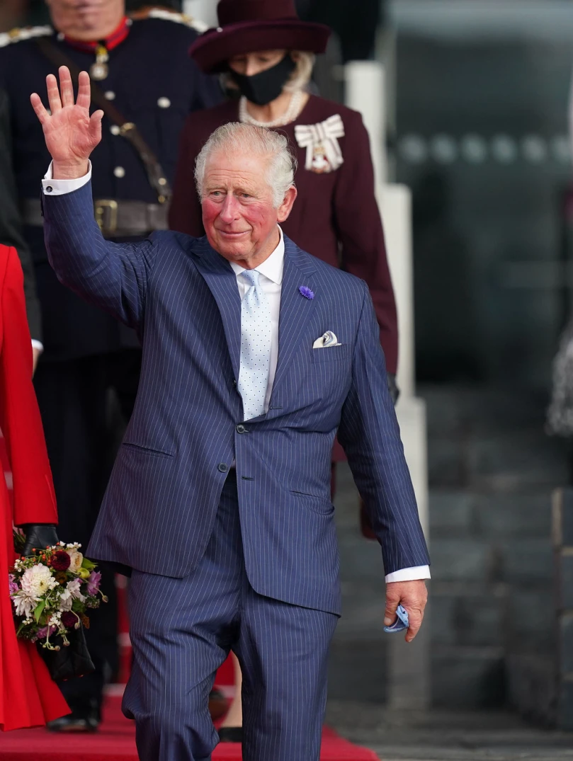 König Charles III. in Begleitung der Königingemahlin geht eine Treppe hinunter und winkt der Menge zu