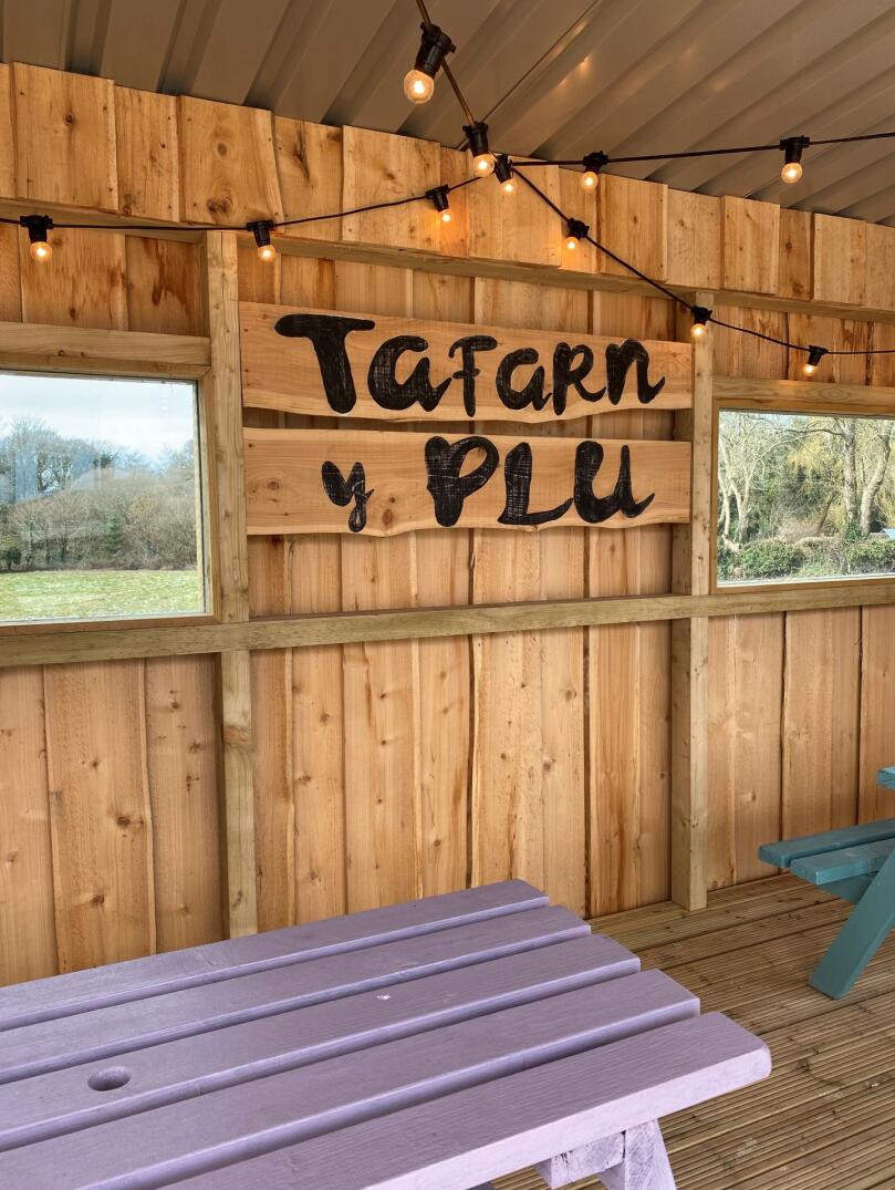 Inside a wooden garden shelter with 'Tafarn y Plu' written on a sign.